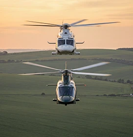 Two helicopters flying over the coutnryside at sunset