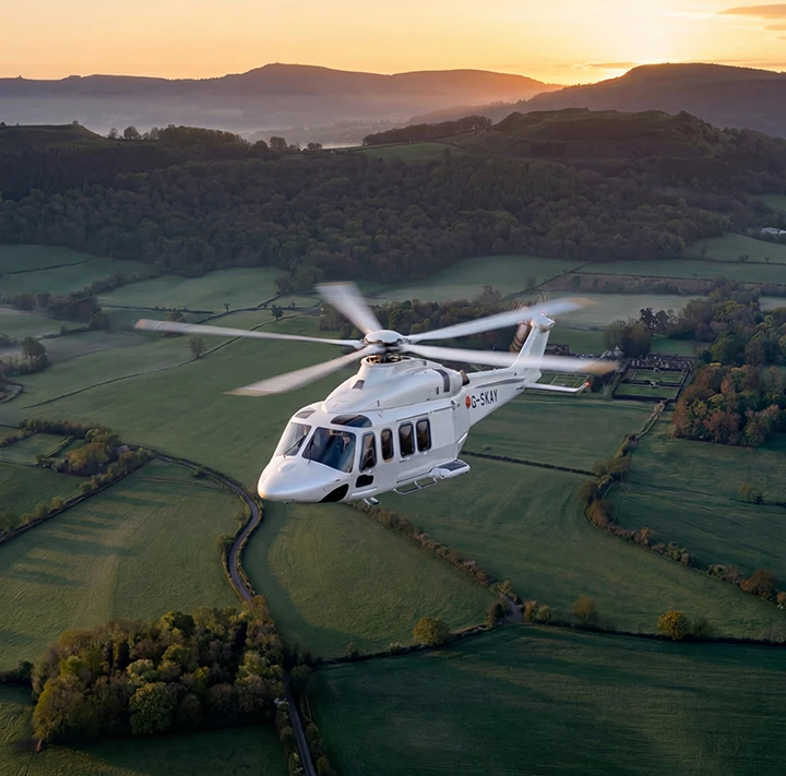 Helicopter flying over fields with a sunet in the background