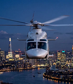 Closeup of a helicopter flying over the thames with the Shard and London skyline lit up in the background